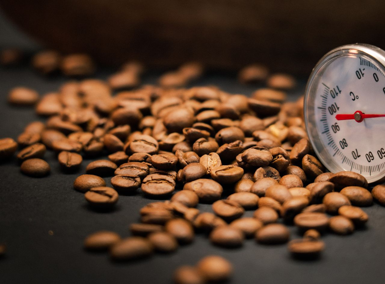 about-us A close-up shot of roasted coffee beans alongside a thermometer indicating temperature.