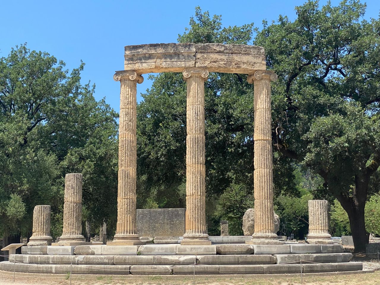 heros-img Explore the ancient Philippeion in Olympia, surrounded by lush greenery under a bright sky.