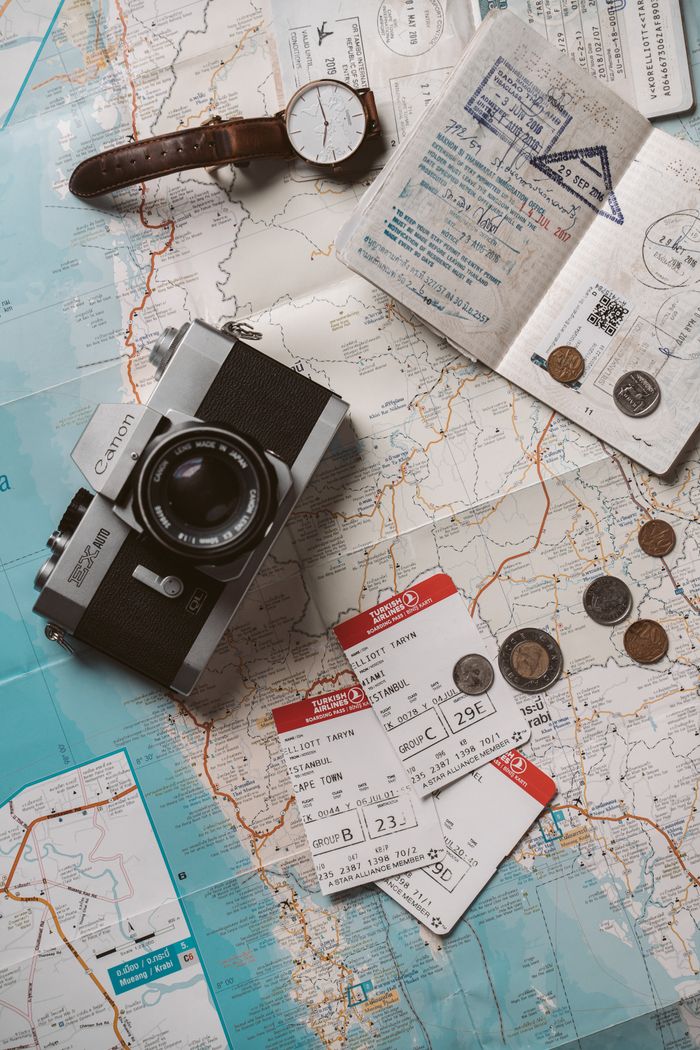 about-us Flat lay travel essentials including passports, tickets, and a vintage camera on a world map.