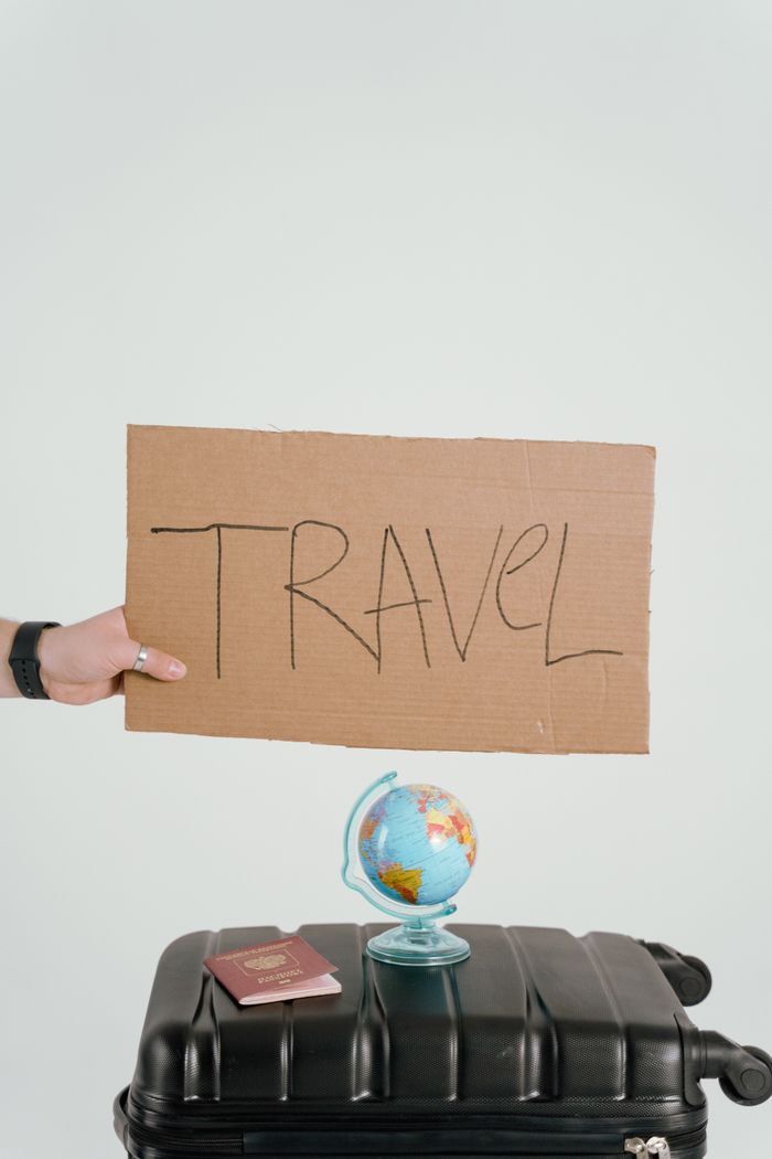 who-we-are Creative travel concept featuring a cardboard sign, globe, passport, and suitcase against a white background.